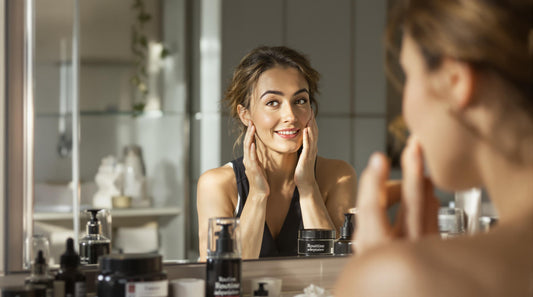 Woman checks her skin in bright bathroom mirror with skincare products