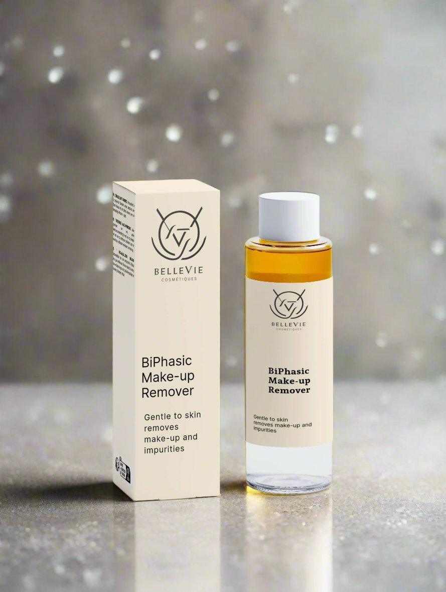 BelleVie BiPhasic Make-up Remover 100ml clear glass bottle and white box on wooden table with warm amber bokeh background, gentle to skin, removes make-up and impurities, COSMOS Natural certified
