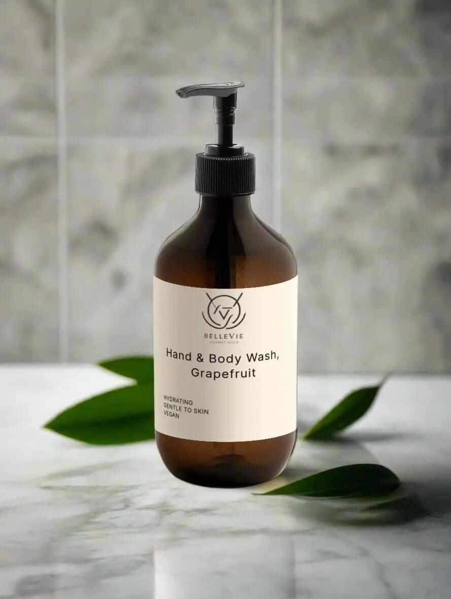 Brown bottle of hand and body wash grapefruti with a label on a marble surface with green leaves.