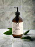 Brown bottle of hand and body wash grapefruti with a label on a marble surface with green leaves.