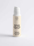 Brightening Face and Body Exfoliator in a cream-colored cylindrical pump bottle with a white dispenser and black label text