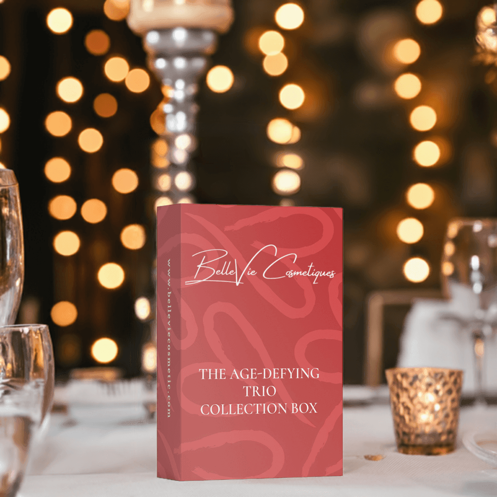 The Age-Defying Trio Collection Box on a table decorated with candlelight, highlighting anti-aging skincare essentials.