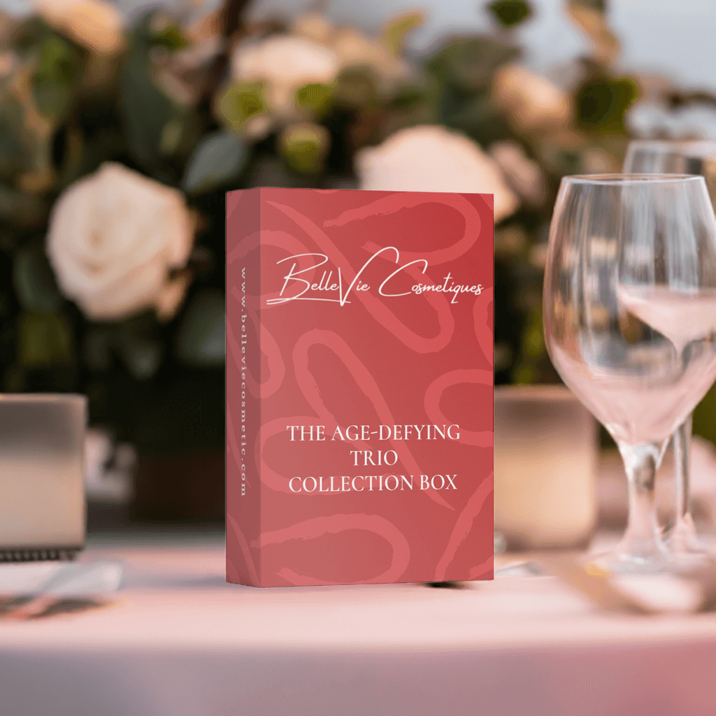 The Age-Defying Trio Collection Box by Belle Vie Cosmetiques displayed on a table with elegant dinnerware.