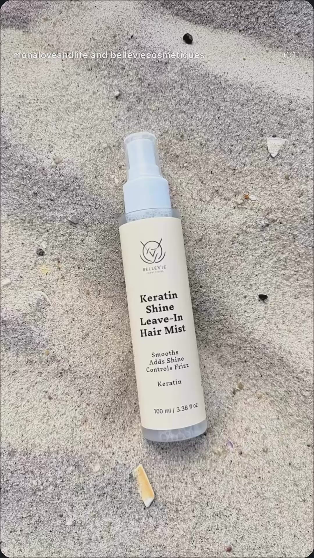 BelleVie Keratin Shine Leave-In Hair Mist 100ml spray bottle lying on sand, with the product label visible.
